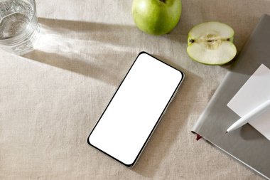 Minimalist zarif yaşam tarzı çalışma alanı, boş beyaz ekranlı cep telefonu şablonu, defter, elmalar ve güneş ışığı gölgeleri tarafsız bej arka planda