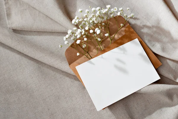 Aesthetic botanical background, empty paper card, envelope with flowers and sunlight shadows on a beige textile background, template with copy space