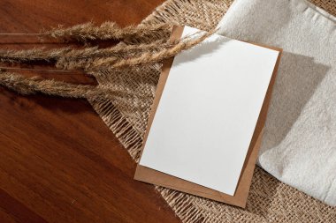 Boş kağıt kart ve kurumuş çayır çimen çivileri ahşap bir masanın üzerinde çiçek gölgeleri, minimalist klasik iş markası, düğün davetiyesi veya tebrik kartı şablonu, kopyalama alanı