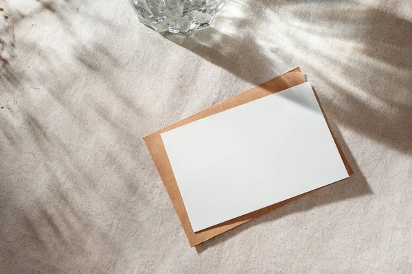 Empty paper card with mock up copy space on a beige table surface with aestethic sunlight shadows, invitation or greeting card, branding template