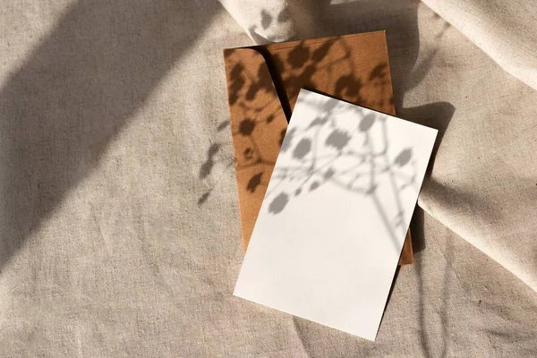 中性ベージュの背景にエレガントな微妙な花の日差しの影を持つ空の紙カードと細工された封筒 コピースペースと審美的なブランドテンプレート — ストック写真