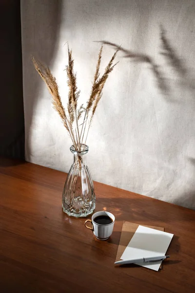 美しい夏のインテリアは 木製のテーブルの上にガラス花瓶のコーヒー 紙のカードと乾いた草の警官とまだ生活 壁に花の太陽の影 朝のビジネスコンセプト — ストック写真