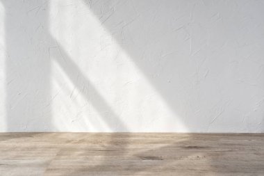 Boş oda tasarım şablonu, beyaz alçı desenli duvar ve güneş ışığı gölgesi olan bej ahşap zemin yüzeyi, ev içi, ürün standı modeli reklam için arka plan, kopyalama alanı