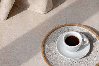 Estetik nötr arka plan, bej taştan bir masada kahve fincanı, güneş ışığı gölgesi, minimalist yaz arkaplanı, kopyalama alanı.