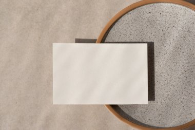 Minimalist ticari marka şablonu, seramik tabakta boş kağıt maketi, bej taşlı arka plan güneş ışığı, düğün davetiyesi veya tebrik kartı tasarımı
