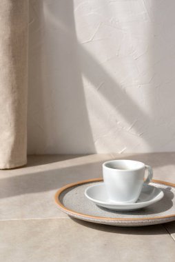 Tabakta kahve fincanı, bej bir masada, yaşam tarzı güneş ışığı gölgesi olan boş beyaz bir duvar arkaplanı, günaydın konsepti, kopyalama alanı.