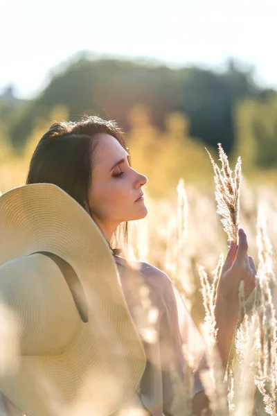 stock image Boho style summer concept, woman portrait at sunset in meadow grass outdoor in nature, holding spikelets in hand, in the end of summer. Blurred soft defocused portrait with backlighting haze.