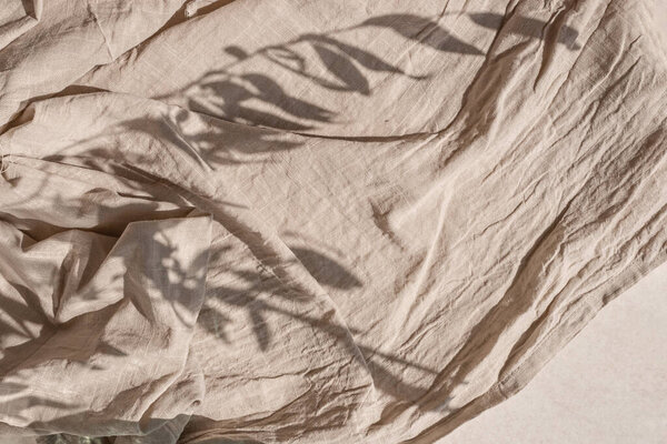 Crumpled linen fabric texture with folds in a sun light and lifestyle floral sunlight shadow. Aesthetic minimal bohemian neutral beige background