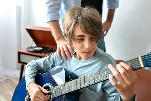 Teenager boy learning to playing an acoustic guitar with father support. Single parent family relations, fatherhood concept. Father support and care, teaching son. Music playing classes.