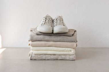 Minimalist pastel, nötr bej, sonbahar örgü kumaş yığını, masada spor ayakkabılar, arka planda beyaz duvar. Estetik moda kadını kostüm, marka ya da blog şablonu