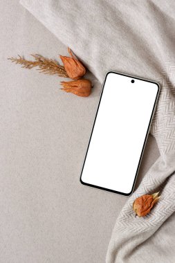 Estetik sonbahar marka şablonu, düz yatış. Tarafsız bej, çıplak renkli, sonbahar zencefilli, turuncu çiçekli tekstil arka planında boş bir cep telefonu modeli..