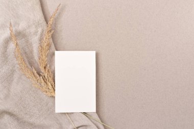 Boş kağıt kart maketi, kurutulmuş çayır çimeni, tarafsız bej arka planda buruşmuş kumaş dokusu, kopyalama alanı. Estetik minimalist güzellik markası, düğün davetiyesi tasarım şablonu