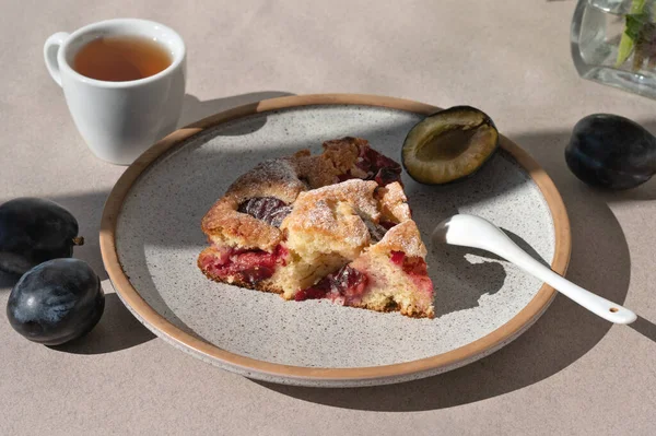 Piece of The New York Times Famous Plum Torte, pie, on plate with teaspoon and cup of tea. Traditional american fruit cake bakery.