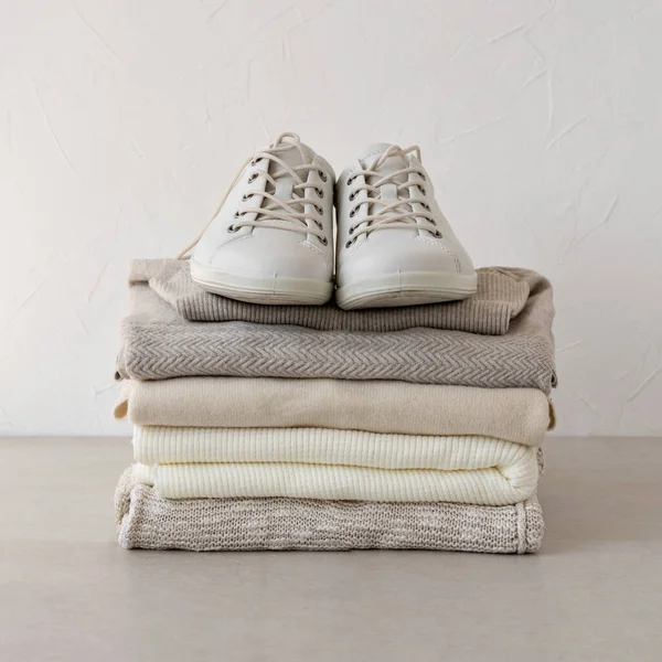Aesthetic fashion woman fall wardrobe, business brand, blog template. Minimalist pastel neutral beige autumn knitwear clothing stack, sneakers on table, on white wall background