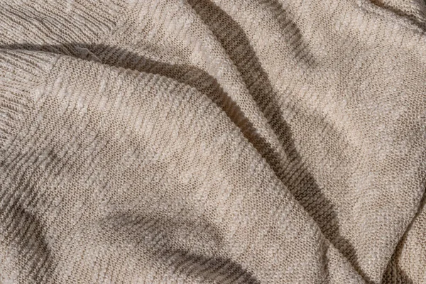 Lifestyle cotton and linen blend knitted jersey fabric background. Messy crumpled neutral beige knitwear texture with sunlight and shadow.