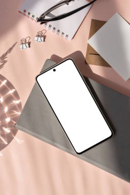 Boş sosyal medya günlüğü şablonu, boş cep telefonu modeli, not defteri, pastel pembe arka plan üzerinde estetik güneş ışığı gölgesi olan kırtasiye.