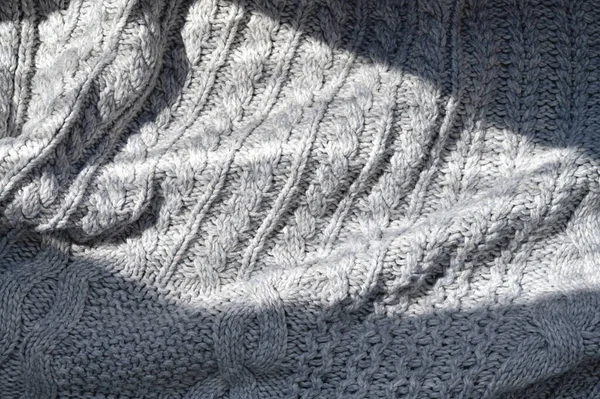 Soft knitted woolen fabric with cable stitch pattern, textured neutral gray autumn or winter cozy background with natural sunlight shadow.