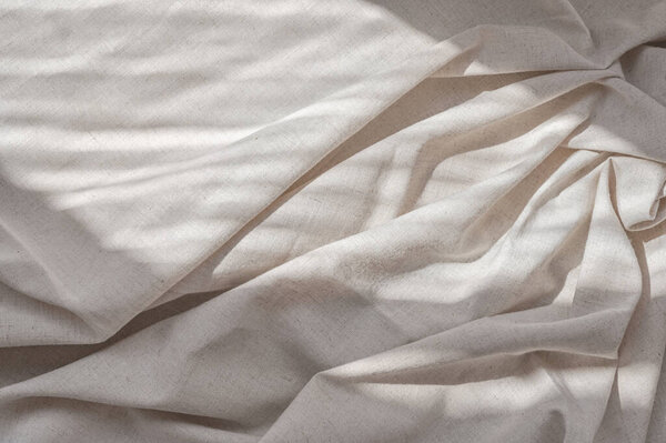 Aesthetic lifestyle bohemian background, business branding template. Crumpled soft neutral beige linen bedsheet fabric texture with folds and natural lifestyle sunlight shadows.