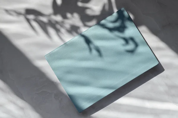 美感简约的中性商业品牌模板 蓝色笔记本或空白封面书籍 挂在白色大理石桌子上 有自然花卉般的阳光阴影 — 图库照片