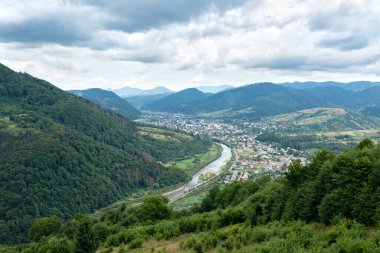 Ukrayna 'nın Ukrayna bölgesindeki Karpat Dağları' nda dağ tepesi, nehir ve iğne ormanı yakınlarındaki otantik bir Ukrayna köyü. Gökyüzü, bulutlar ve hava manzaralı manzara..