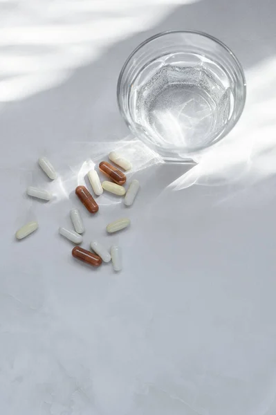 Beyaz ve kahverengi ilaç kapsülleri, haplar, vitaminler ya da takviyeler ve beyaz masa arkaplanında fotokopi alanı olan su dolu camlar. Sağlık, sağlık, ilaç endüstrisi yaşam tarzı konsepti.