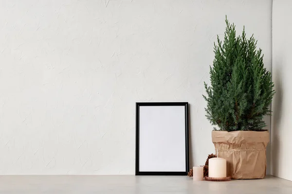 Minimal Nordic white winter home interior design template. Blank picture frame, juniper in pot, candles on beige table and empty white wall background.