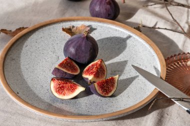 Tam ve incir meyvesini tabakta bıçakla, bej keten masa örtüsünde. Doğal güneş ışığı gölgeli yaşam tarzı kompozisyonu. Sonbahar tatlısı, vitamin ve lif sağlıklı beslenme için.