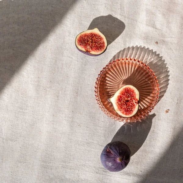 Minimal autumn background with fig fruits on linen tablecloth and harsh aesthetic sunlight shadows.