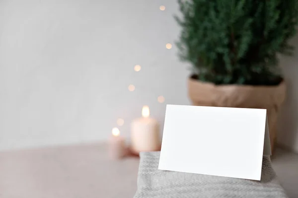 空白纸制卡片的模型 桌上的毛衣 模糊的焦点蜡烛和花环灯 背景在壶中的Juniper 空的中性米色墙壁复制空间 圣诞明信片或邀请函模板 — 图库照片