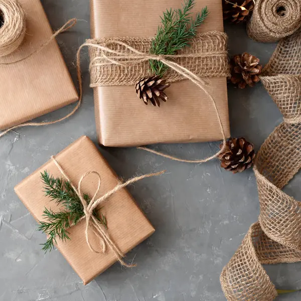 Christmas sustainable holiday celebration background, crafted brown gift boxes, decorated with pine tree branch and cone on gray table background. Making aesthetic winter presents in rustic style.