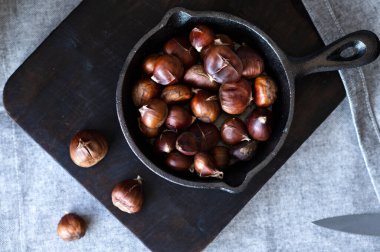 Kahverengi kavrulmuş kestaneler, koyu ahşap tahtada tavada. Geleneksel Noel kış ziyafetlerinin ev yemekleri, Avrupa 'nın otantik mevsimlik yemekleri.