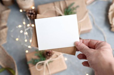 Noel kartı maketi ve zarf hazırlandı. Masanın üstünde, üzerinde çözülmüş hediye kutuları ve çelenk ışıkları var. Estetik yaşam tarzı iş marka şablonu.