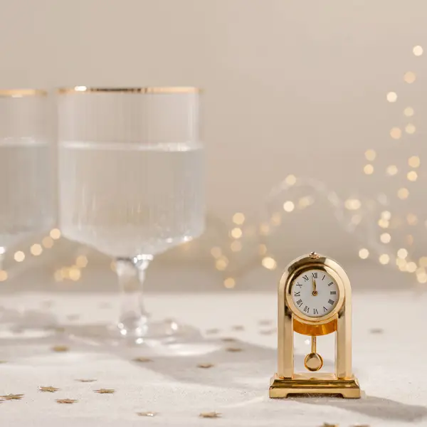 新年假期庆祝的概念 黄金古董时钟显示12点钟 酒杯与灿烂的葡萄酒 模糊的花环灯背景 审美中性的节日背景 — 图库照片