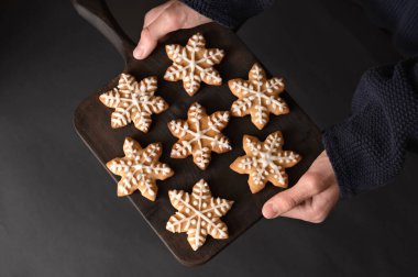 Elleri ahşap tahta, yıldız kurabiyeleriyle süslenmiş, koyu arkaplanda şekerle süslenmiş. Geleneksel Noel ziyafeti, yemek. Yumuşak seçici odak, yaşam tarzı.