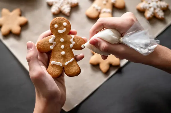 Christmas gingerbread man cookie decoration with sugar icing. Person\'s hands holding gingerbread man cookie and piping bag with sugar icing, making ornament. Holiday homemade family bakery.