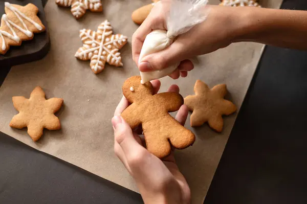 Making decoration of gingerbread man cookie from piping bag with sugar glaze.