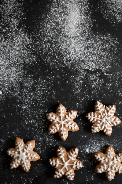 Black table background with flour and star gingerbread cookie decorated with sugar glaze, top view, copy space.