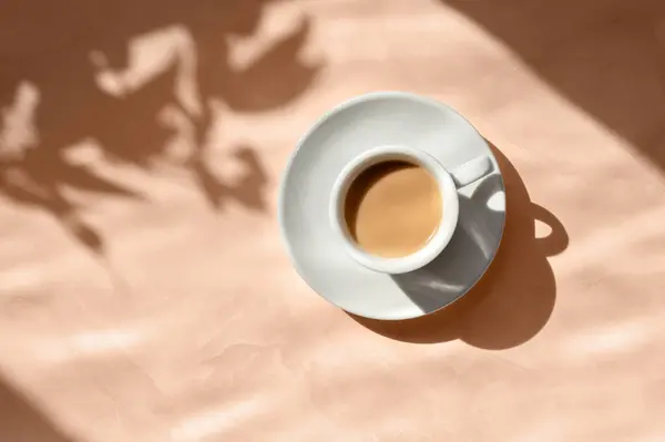 Aesthetic floral sun light shadows and coffee cup on peach table background. Good morning concept in trendy color 2024.
