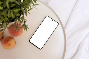 Cep telefonu boş ekran maketi, şeftaliler yatağın yanında, kırışık beyaz yatak, yatak odasında günaydın, yaşam tarzı..