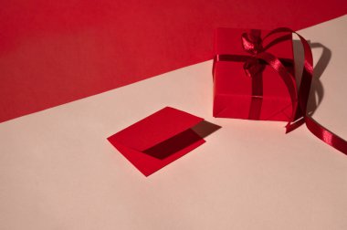 Kırmızı hediye kutusu ve pastel şeftali üzerine kağıt kart ve parlak ışık ve sert gölgelerle kırmızı geometrik arka plan. Lüks yaratıcı tatil kutlamaları arka planı, minimal ticari marka şablonu.