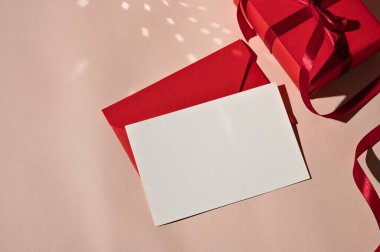 Şatafatlı kadınsı tebrik kartı şablonu, boş kağıt maketi, kırmızı zarf ve parlak ışık ve gölgeli pastel pembe arka planda hediye kutusu. Tatil kutlaması arkaplanı.