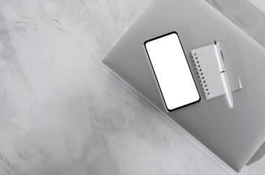 Minimum zarif ofis çalışma alanı, kapalı dizüstü bilgisayar, boş ekran maketi olan cep telefonu, defter, yumuşak güneş ışığı gölgeleri, düz yatay, üst görünümü olan nötr gri mermer masa üstü arka planı kalem.
