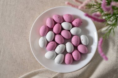 Tabakta küçük pembe ve beyaz yumurta şekilli şekerler, nötr bej masa örtüsü arka planında, Paskalya bayramı tatlıları ve dekor.