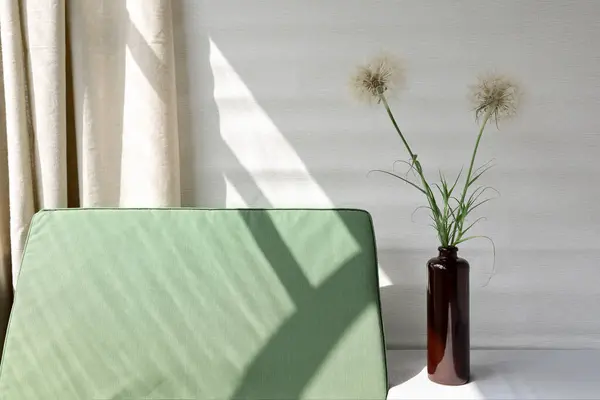 Minimal spring summer home decor, vase with dandelion flowers, green textile chair with natural aesthetic sun light shadows, beige linen curtain, aesthetic sustainable still life.