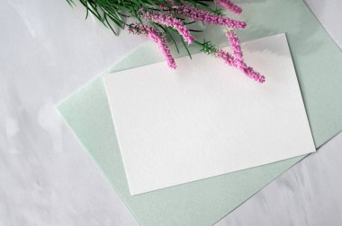 Bahar estetik tebrik kartı veya davetiye şablonu, boş kağıt kart, pembe çiçekler, nötr mermer masa zemininde açık yeşil kırtasiye, düz uzanmış.