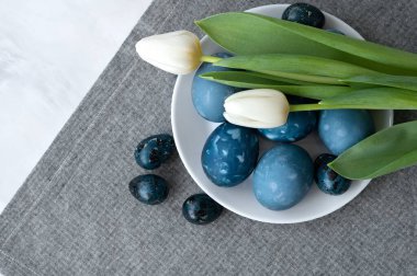 Mavi boyanmış Paskalya yumurtaları ve gri keten peçete arka planında lale çiçekleri, Paskalya bayramı kompozisyonu, İskandinav tarzı.