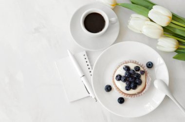 Tatlı tatlı ve kahve fincanı, boş kağıt defter, beyaz masa zemininde kalem ve çiçekler. Kalori hesaplama, sağlıklı beslenme, diyet planlama..