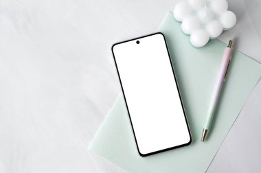 Boş ekran maketli cep telefonu, beyaz nötr mermer masa arkaplanı üzerine pastel yeşil kağıt kağıt kırtasiyesi doğal güneş ışığı gölgeleri, sosyal medya için estetik şablon..