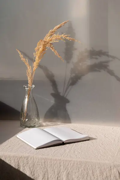 審美的な小麦の夏はまだ生命 家の内部の装飾 開いた本 砂のベージュのリネンのテクスチャされたテーブルクロスが付いているテーブルの乾燥した草が付いている花瓶 粗い自然な日光の影 — ストック写真