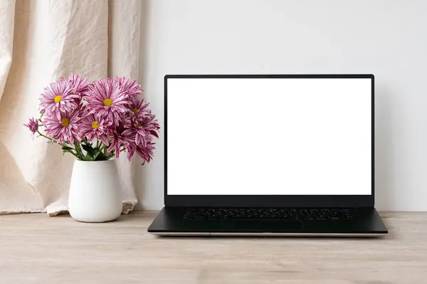 Laptop boş ekran modeli, bej ahşap masa üzerinde pembe papatya çiçekleri olan vazo, beyaz duvar ve keten perde arka planı, estetik iş modeli, kopyalama alanı.